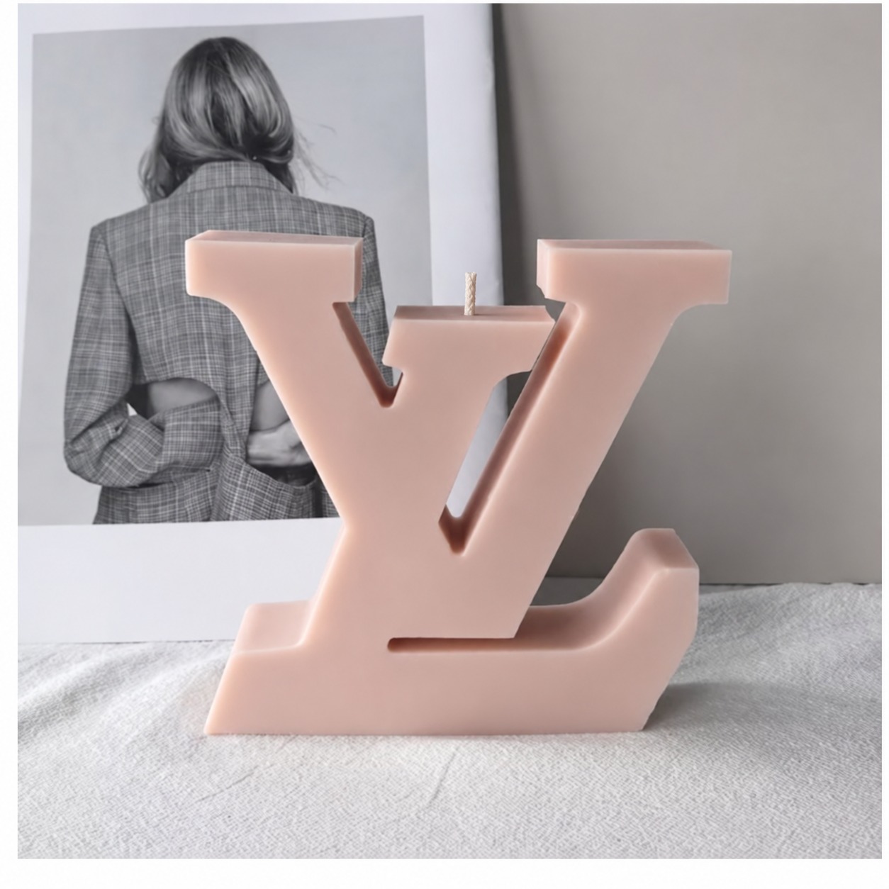 Blush pink sculptural letter candle displayed on white fabric
